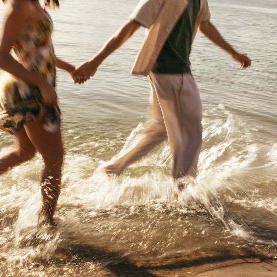 Et par på stranden holder hinanden i hånden mens de løber langs vandkanten.