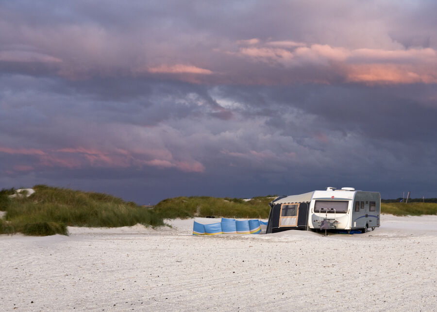Billede af campingvogn på en strand, med mørke skyer i baggrunden