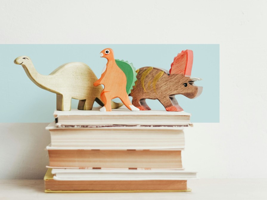 Tre dinosaur-træfigurer står oven på en stak bøger.