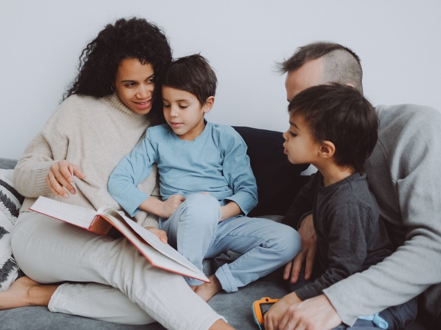 Familie sidder sammen i sofaen og læser en bog højt.