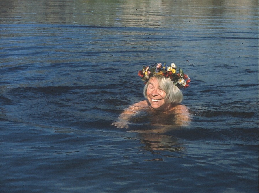 Tove Jansson svømmer i vand med blomsterkrans